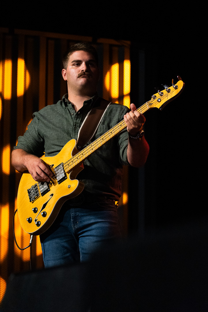Tanner “Rooster” Barnett playing a gold bass under amber stage light